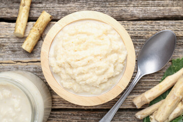 Tasty horseradish sauce, spoon and roots on wooden table, flat lay