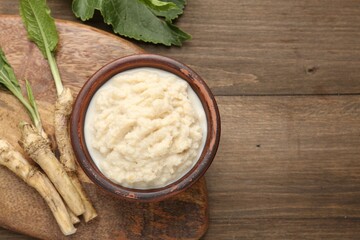 Tasty horseradish sauce and roots on wooden table, flat lay. Space for text