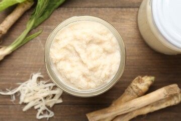 Tasty horseradish sauce and roots on wooden table, flat lay