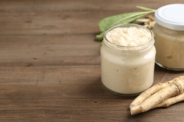 Tasty horseradish sauce and roots on wooden table, closeup. Space for text