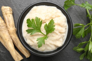 Tasty horseradish sauce with parsley and roots on black table, flat lay