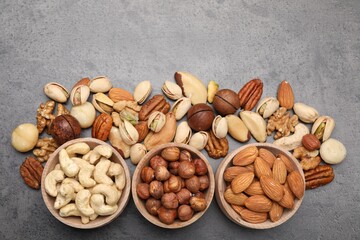 Mix of different nuts in bowls on grey table, flat lay. Space for text
