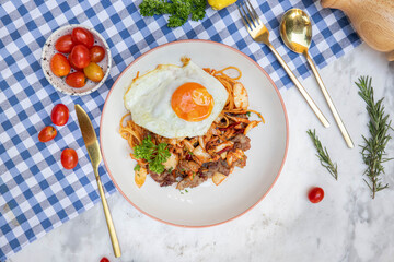 A Culinary Canvas: A top-down image captures a vibrant plate of gourmet pasta, with a flawlessly fried egg atop a bed of succulent meat and fresh vegetables. The dish, set on a checkered table.