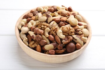 Mix of different nuts in bowl on white wooden table, closeup