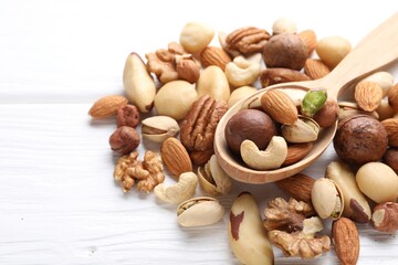 Mix of different nuts and spoon on white wooden table, closeup. Space for text