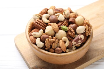 Mix of different nuts in bowl on white wooden table, closeup