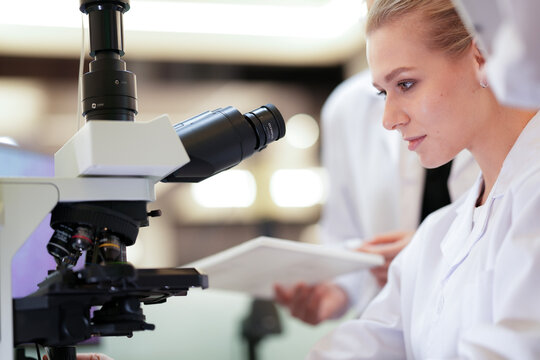 A team of medical researchers discusses their experiment's results. They are analyzing data and microscope findings together in a clinical laboratory to reach a conclusion. - Powered by Adobe