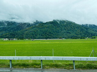 Fototapeta premium Scenic Swiss countryside with mountains, green fields, and a passing train