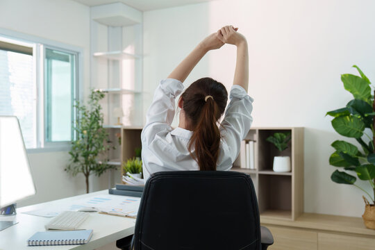 Workplace Comfort. Young woman stretching in office chair to relieve tension and promote well-being.
