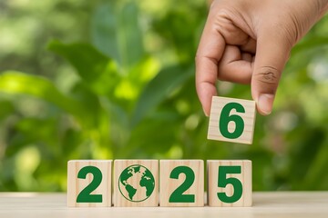 Hand placing a wooden block with the number six on top of a sequence of wooden blocks spelling out the year 2025 with a green earth icon representing environmental sustainability and future planning