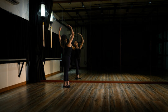 Elegant dancer performing ballet poses in front of a large mirror under dramatic lighting