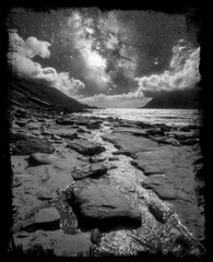 Black and white landscape with rocky beach and starry sky