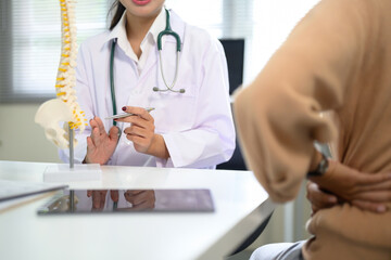 Patient holding lower back while doctor provides advice with anatomical spine model