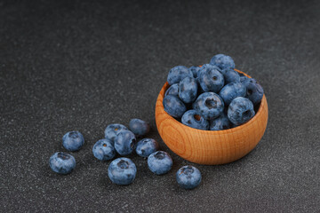 Fresh ripe blueberries in small wooden bowl on dark gray textured stone background. Delicious organic fruit rich in vitamins, wild berries,healthy lifestyle, natural food. Close up, macro