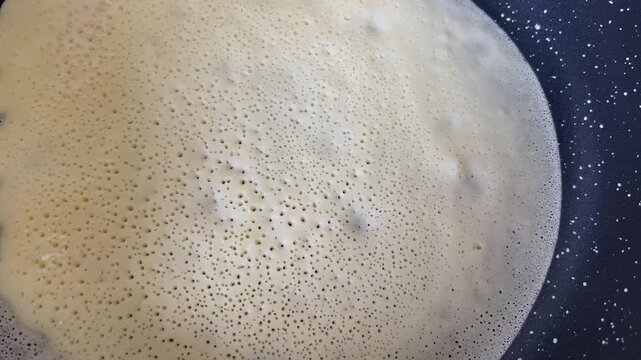 Blini cooking on a pan with visible bubbles in the batter. Concept of traditional Russian pancakes, Slavic cuisine, and Maslenitsa celebration