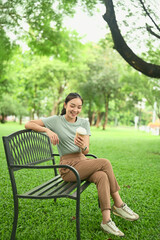Fototapeta premium Happy young woman in casual outfit enjoying a hot drink while sitting outside in a peaceful natural