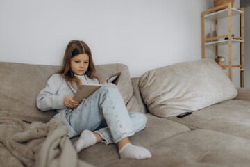 Young Girl Relaxing on Sofa Reading a Book at Home