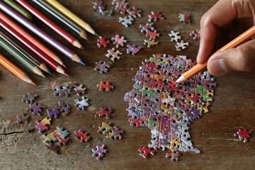 Jigsaw puzzle of a human head, colored pencils, and a hand holding a pencil