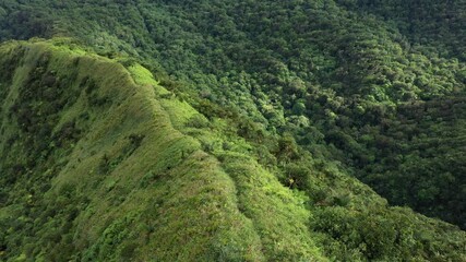 Steep mountain ridge covered in green vegetation overlooking dense tropical forest valley below