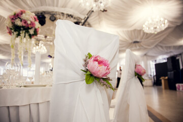 Elegant wedding chair decorations with peonies and white draping in a banquet hall setting