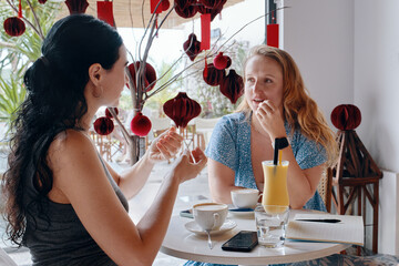 Two young womens friends sitting by table in cafe with variety of drinks, having chat and coffee.
