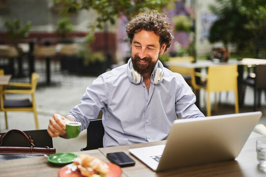 A focused man engages in work activities at a cafe, enjoying a cup of espresso while seated at a table with a laptop and snacks. The atmosphere is relaxed and productive. - Powered by Adobe