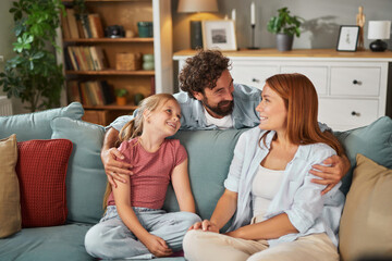 A family enjoys a warm day in their living room, sharing smiles and laughter. The relaxed atmosphere is complemented by colorful cushions and comfortable seating.