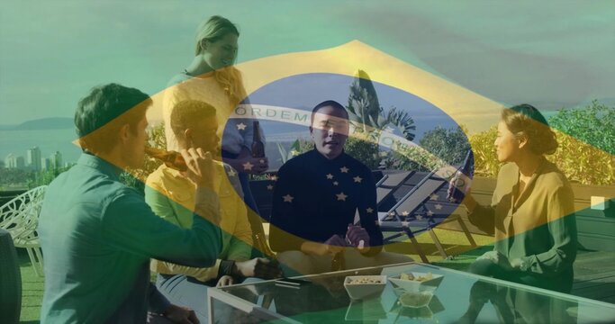 Chatting five friends sitting around glass-top table on rooftop terrace, with snacks and drinks