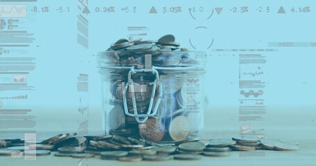 Fototapeta premium Transparent glass jar holding assorted coins on wooden surface in studio, with blue graphs