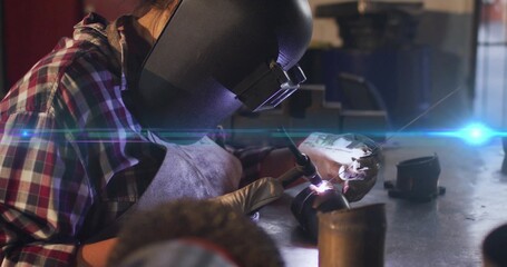 Welder wearing helmet and gloves, welding pipe fitting with torch in workshop, sparks flying