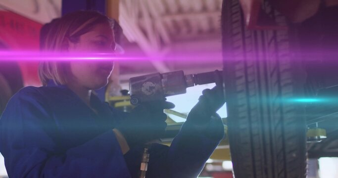 Technician in blue coverall using air impact wrench loosening lug nuts on car wheel in workshop