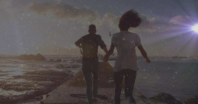 Running couple holding hands along concrete jetty at sunset, crashing waves on rocks and seabird - Powered by Adobe