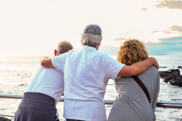 Back view of group of senior friends enjoying a scenic ocean view together leaning on a seaside railing. Three adults embodying themes of friendship, active retirement, and coastal lifestyle © luciano