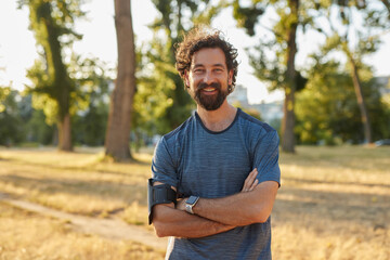 A man stands confidently with arms crossed in a city park as the sun sets, embracing a healthy...