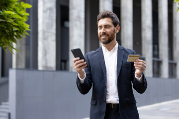 Smiling businessman holding credit card and using smartphone for online shopping or banking...