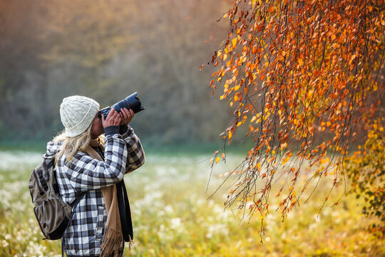 Woman with camera photographing autumn nature enjoying hiking and outdoor lifestyle exploration in fall season