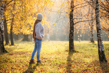 Woman in sweater walking in autumn park among birch trees enjoying sunny day in fall season nature and fresh air outdoors