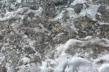 Stones under water. Sea foam. Natural background. Stone texture. Abstract background with pebbles. Pebble beach near Afandou village, Mediterranean Sea, Rhodes Island, Greece. Summer and holidays.  