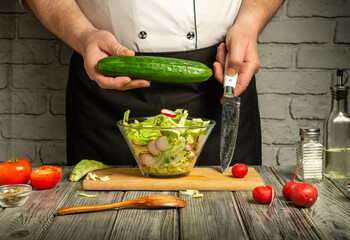 A chef skillfully chops vegetables, including a cucumber, while preparing a fresh salad in a cozy...