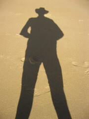 A striking shadow of a man in a hat cast beautifully on the ground