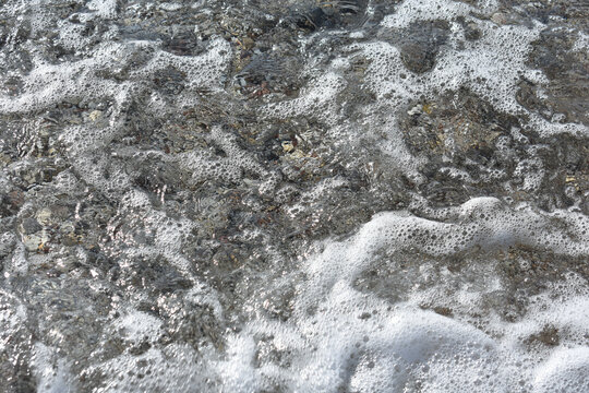 Stones under water. Sea foam. Natural background. Stone texture. Abstract background with pebbles. Pebble beach near Afandou village, Mediterranean Sea, Rhodes Island, Greece. Summer and holidays.  