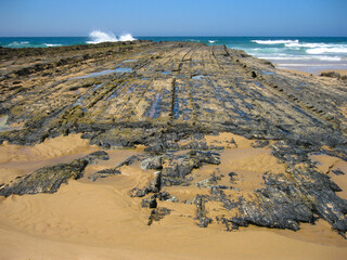 A sandy beach with rocks and crashing waves in the background