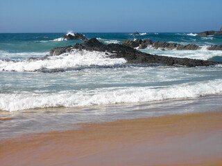Waves crashing on a sandy beach with rocks create a serene vibe