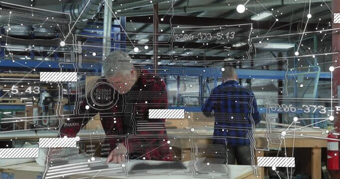 Woodshop designer unfolding blueprint and launching data overlay while colleague stacking panels