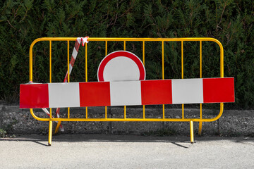 A temporary yellow road barrier features a prominent red and white striped warning board and a 