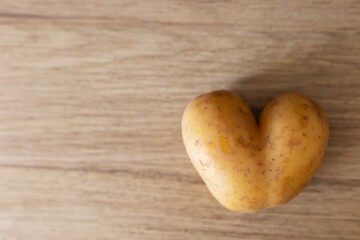 A unique heart-shaped potato rests on a smooth wooden table, showcasing its distinct shape and texture. The simple setting adds warmth, making it an intriguing sight for food lovers