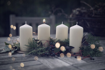 First burning advent candle with christmas decoration and golden bokeh on a terrace at dusk. Christmas background with space for text.