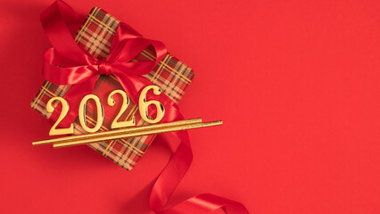 Beautiful festive gift with a ribbon and a bow in honor of the New Year 2026 celebration on a red flat simple background.
