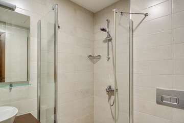 A spacious modern bathroom with a clean design, featuring a glass shower, a wooden vanity unit, and tiled walls. The elegant fixture placement creates a comfortable and functional space.