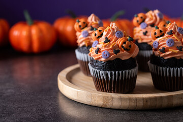 Halloween cupcakes with Halloween sprinkles on black surface and purple background. Copy space